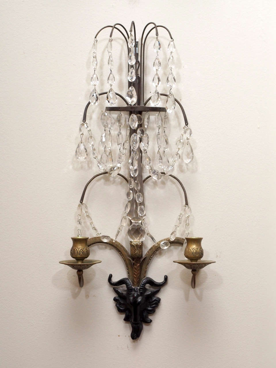 A pair of tall, crystal wall lights, the metal (likely bronze) hand etched, the crystals hand cut, with finely molded and chased ebonized rams heads.   Not electrified.