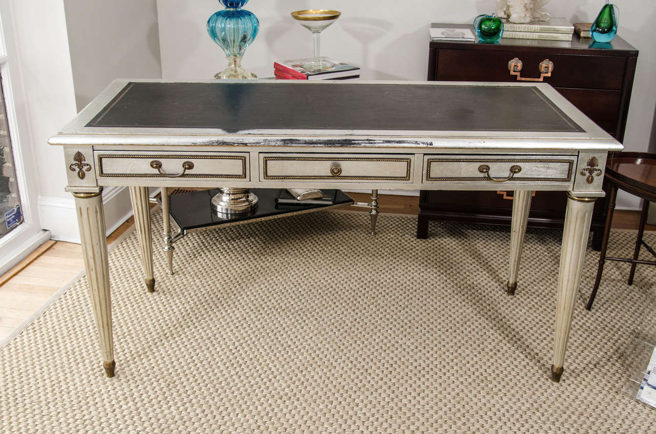 A glamorous take on a traditional piece, this French silvered desk has fluted legs, brass detailing and a black tooled leather top.