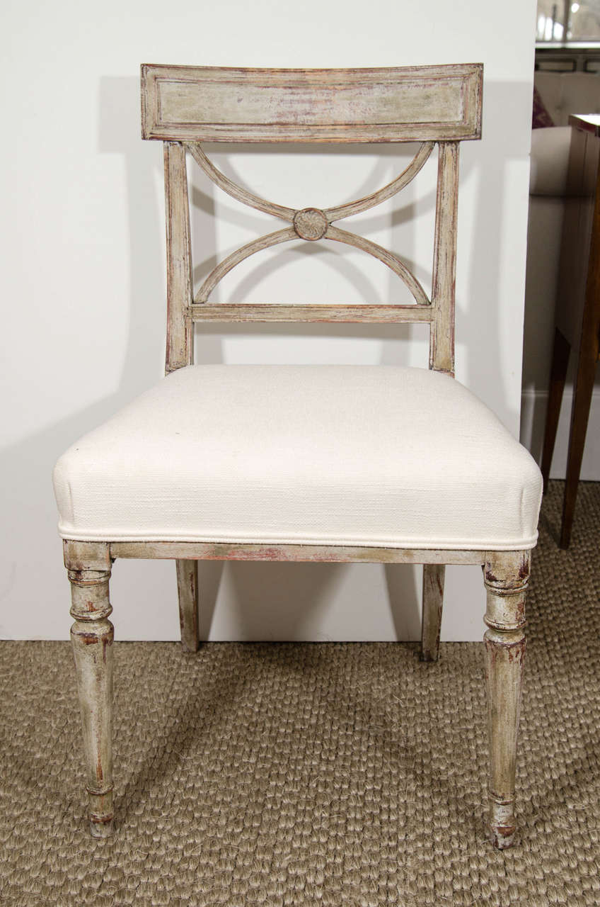 A charming and elegant set of eight painted dining chairs from Sweden, with a carved back splat, turned and slightly tapered legs and covered in a cream linen.