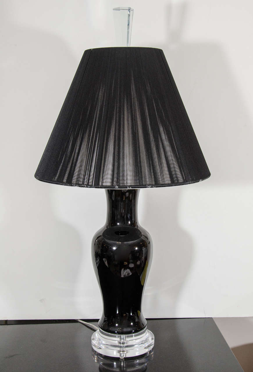 A simple and sleek black ceramic urn-shaped lamp with a Lucite base and a black string shade.
