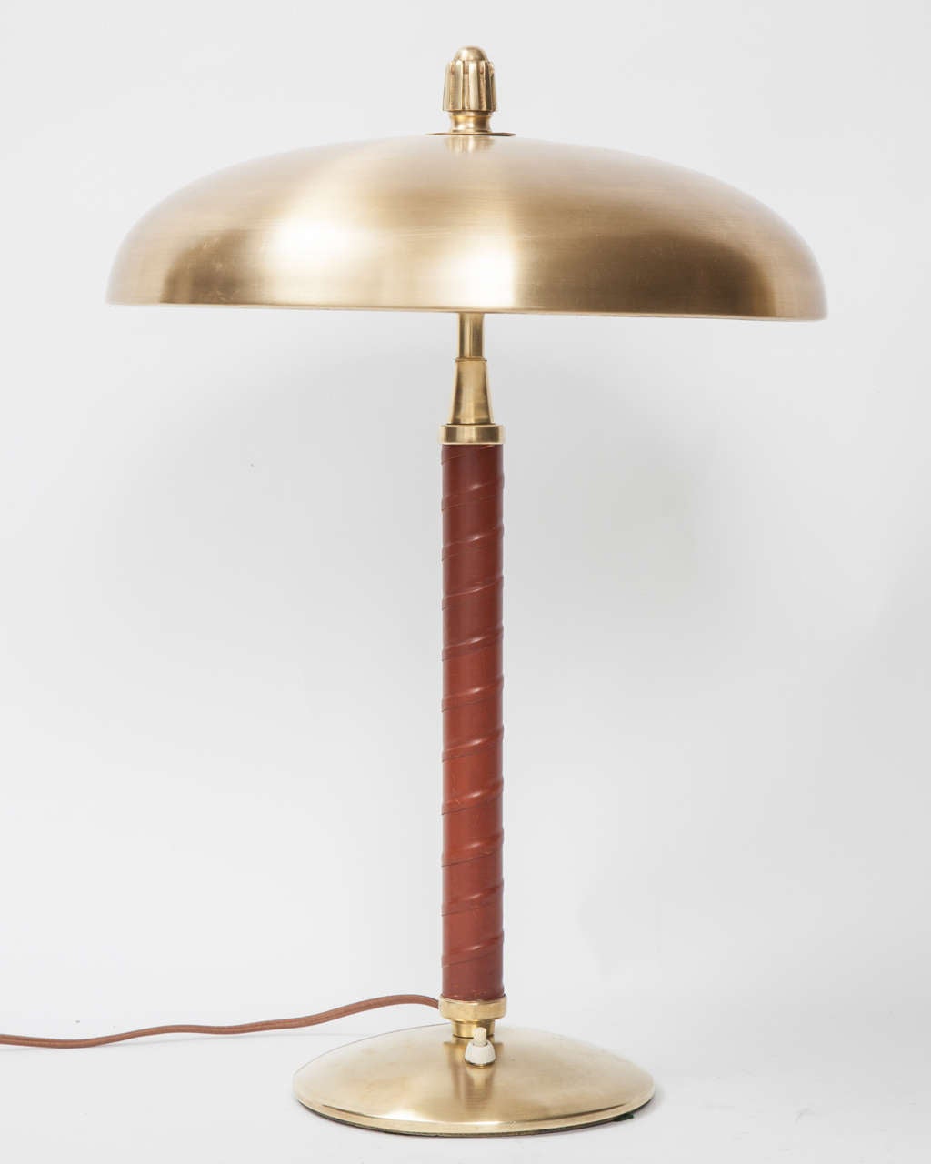 A Swedish Modern table lamp, Circa 1930-1940, with a polished brass dome shaped shade surmounted with a fluted finial, leather wrapped stem and circular brass base. Probably made by Einar Bäckström Metallvarufabrik, Malmo. or Zenith Rewired to US