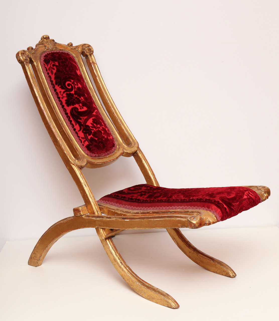 More sculpture than furniture, this finely-carved 1860s folding chair has a gilded and gessoed wood frame, and the original cut-silk-velvet upholstery material that was woven to fit. A fine example of the offbeat, fetishistic quality that typifies