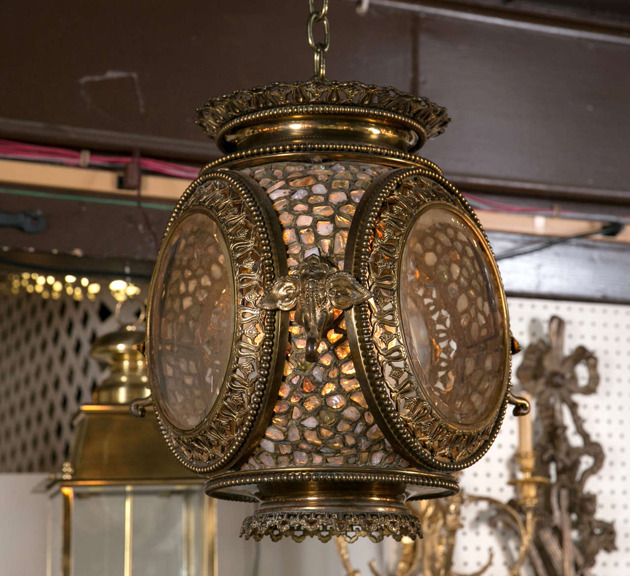 This hanging lantern has three sides of beveled glass with an open fretwork frame. The surrounding areas are of translucent stones within brass. There are three elephant heads between the beveled glass and open fretworks frames.
The bottom did have