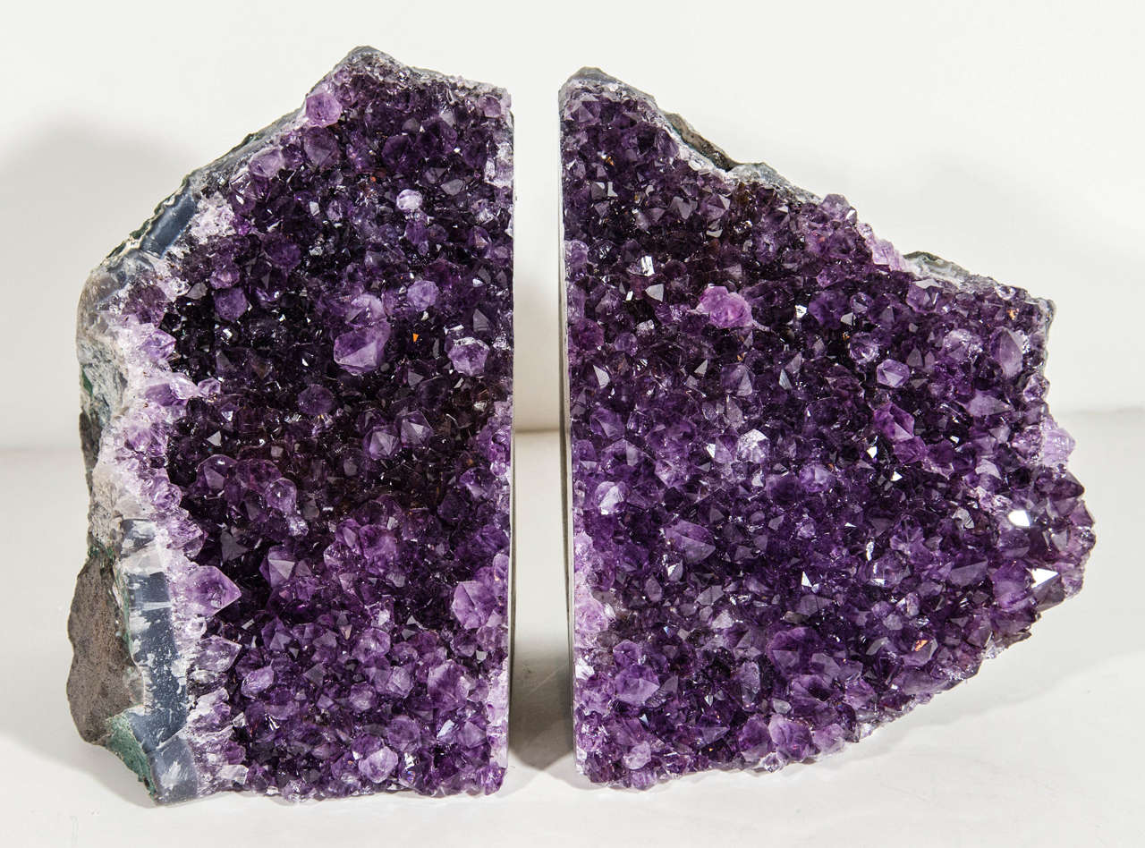 Pair of outstanding large amethyst geode bookends and/or sculptures. The specimens features rough stone edges in hues of slate with variant green edges, and a multitude of vibrant amethyst crystalized spikes in deep purple.  Each bookend measures
