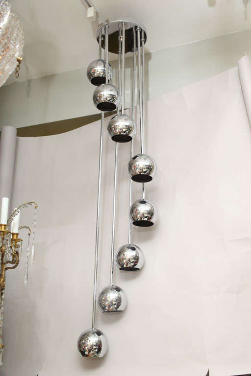 An 8 light American ceiling fixture with a round ceiling plate issuing rods of graduating length, undulating to lowest tier and each rod having spherical chrome element housing Edison socket.