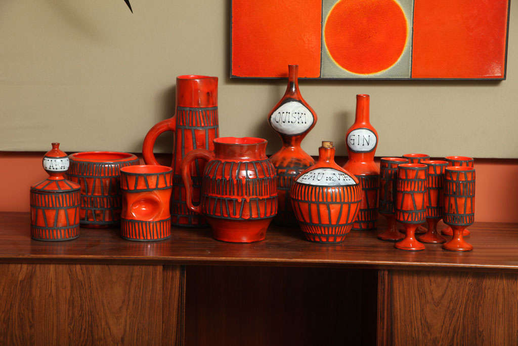 This set, quite rare, is also among the most distinctive in Mr. Capron's repertoire of ceramic vessels, featuring a fierce red enamel glaze and bold linear friezes.  Produced from molds, Capron next used a lost-wax method, sketching the motifs on