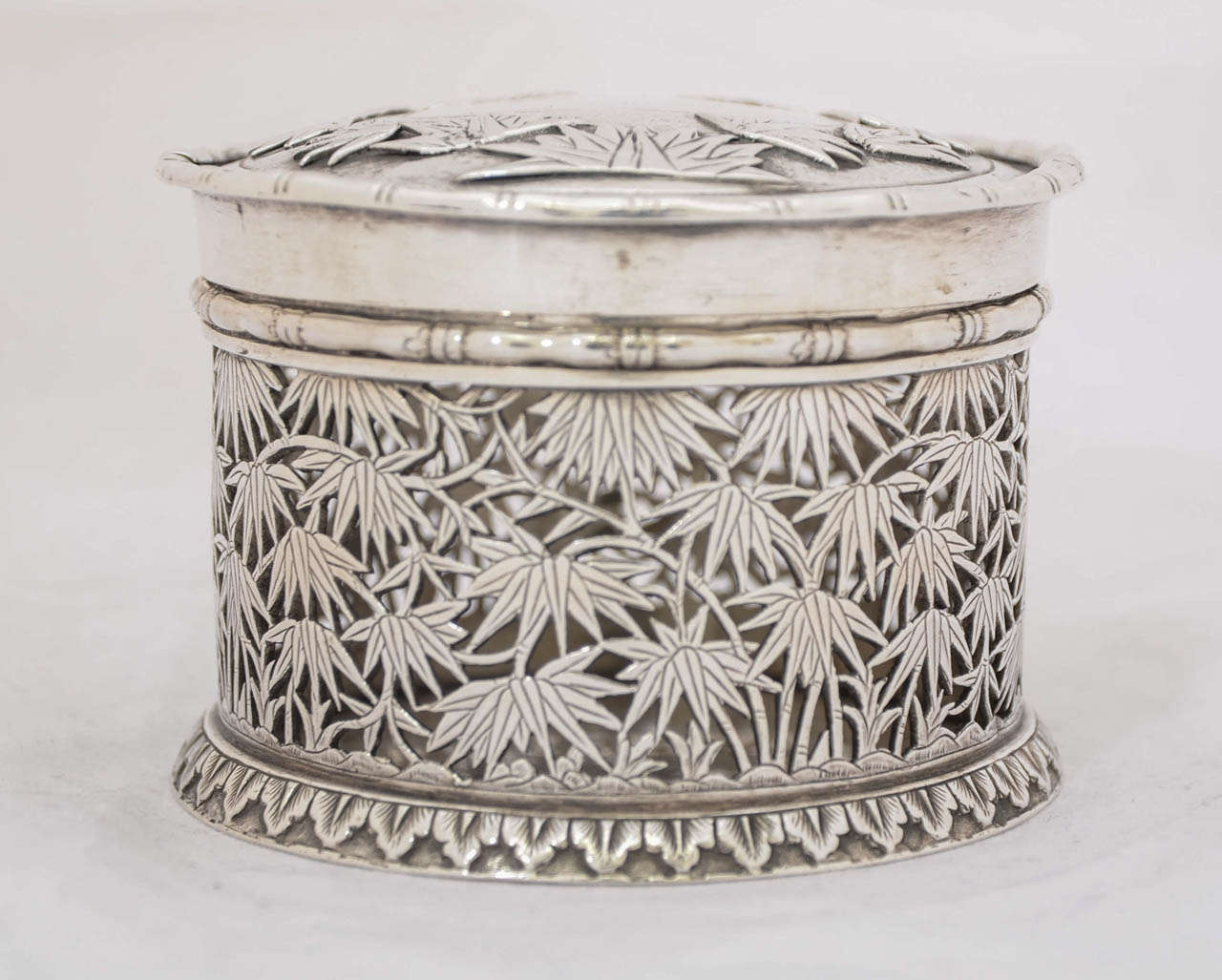 A Chinese export silver box of round form, pierced sides, and pull-off lid. The decoration is of bamboo and there is a plain shield on the cover. The box is heavier than is usual for this type, weighing 216 gm. It is 6.5 cm high and the diameter is