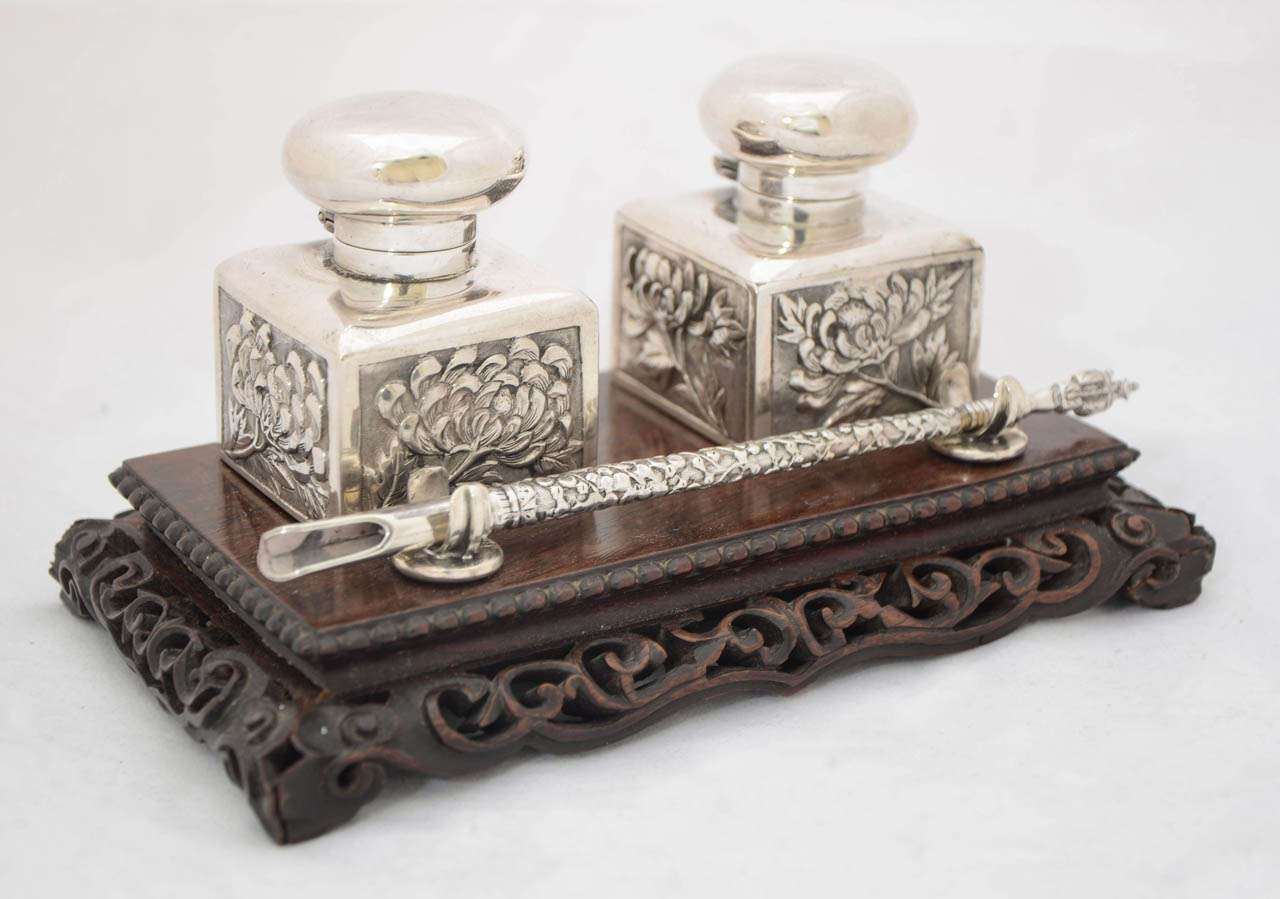 A Chinese Export Silver and wood Inkstand with dip-pen dating from around 1885. The hinged ink bottles are decorated with embossed chrysanthemum to the sides and the covers are plain. The pen has a figural end and it is a perfect size to complement