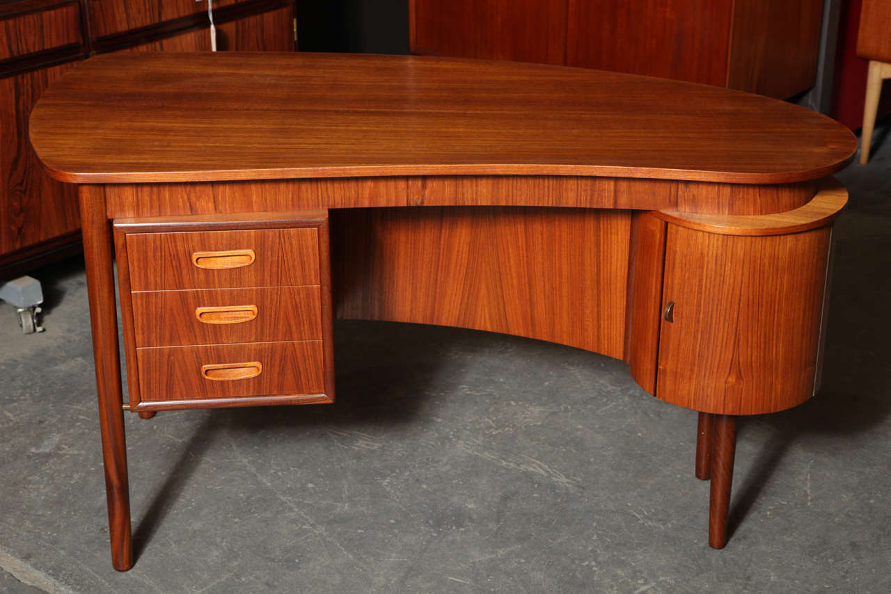 Dainty paisley-shaped teak desk with 3 drawers, bar cabinet with a semicircuclar brass pull, and open shelves.  Well-suited for a small office or studio.