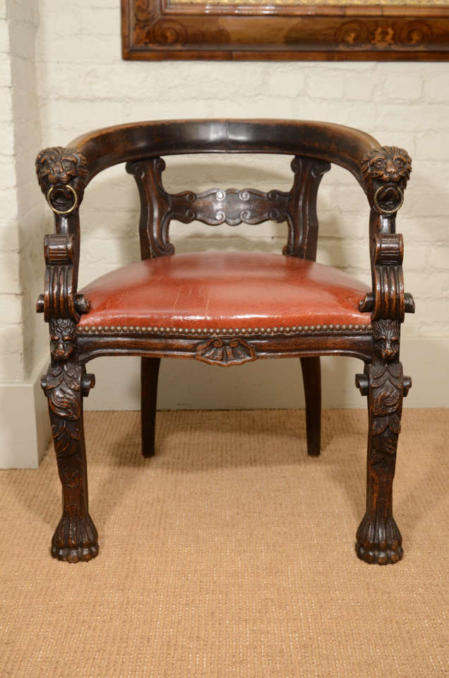 The curved back rail over a scroll carved back splat. The back rail terminating in carved lion heads with brass rings over reeded s-scrolls. The chair supported by mask and foliage carved front legs with stylized paw feet and in-curved back legs.