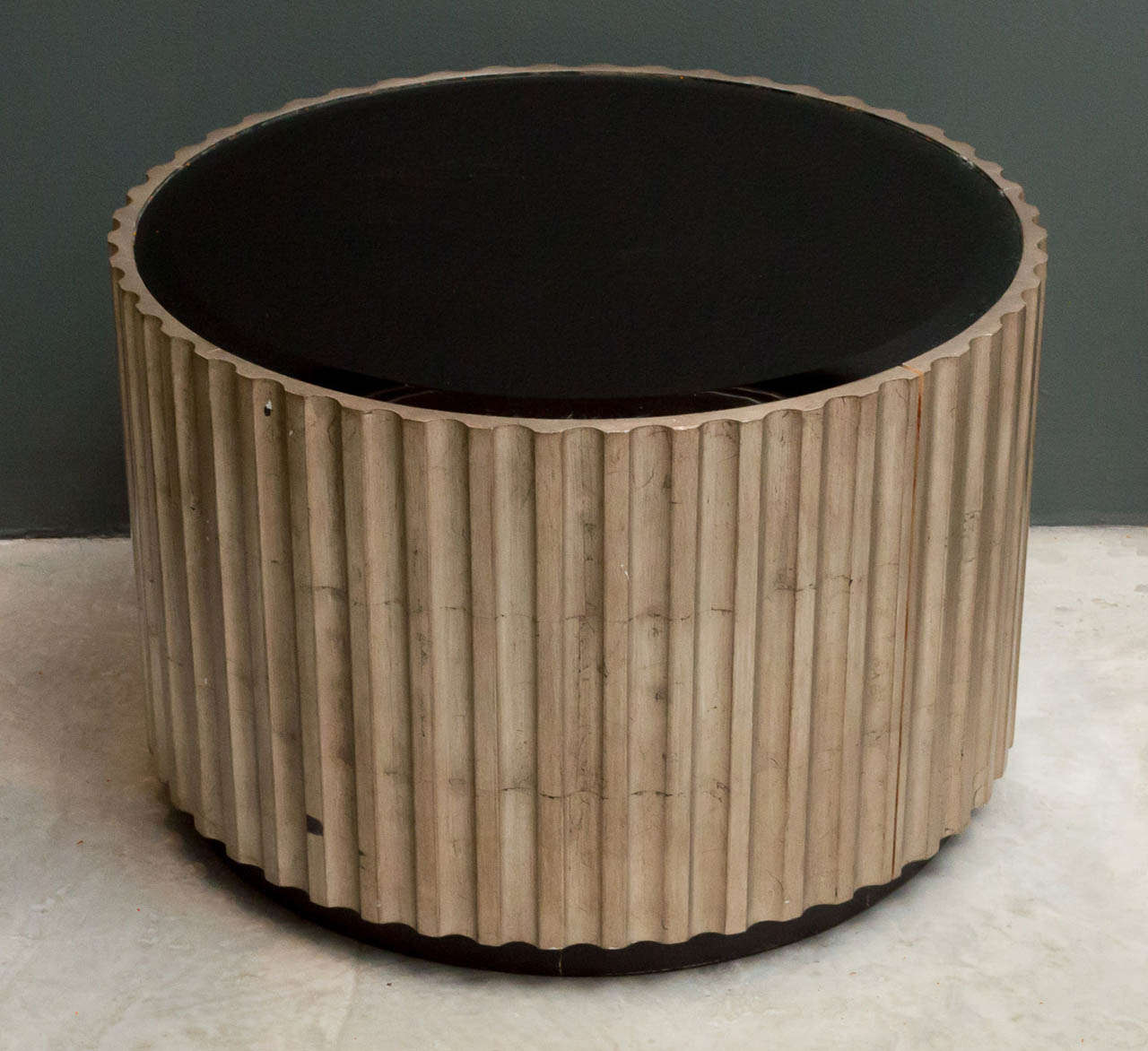 Mid-20th century hand carved fluted circular low table in antique silver leaf with inset black glass top on recessed base.