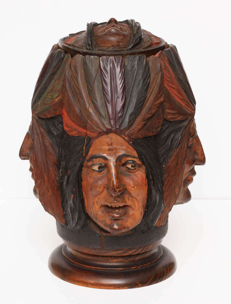 Various hand-carved Indian Chief faces adorn the sides of this tobacco jar. Very detailed with interesting facial expressions and each wearing a colorful feather headdress. Fitted with a lidded top which also has an Indian face carved onto the