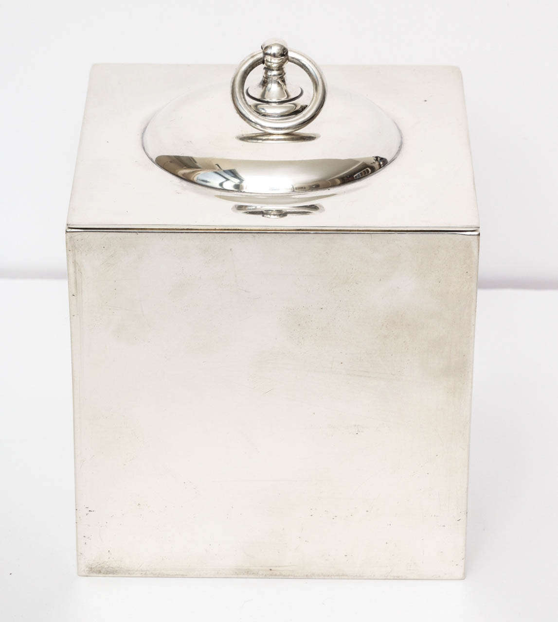 An interesting cube shaped box by Tiffany & Co. The lid is detailed with a raised circular center and a round pull top. The interior is lined with wood. This piece has a nice weight and is very well made. The seams are not noticeable at all which