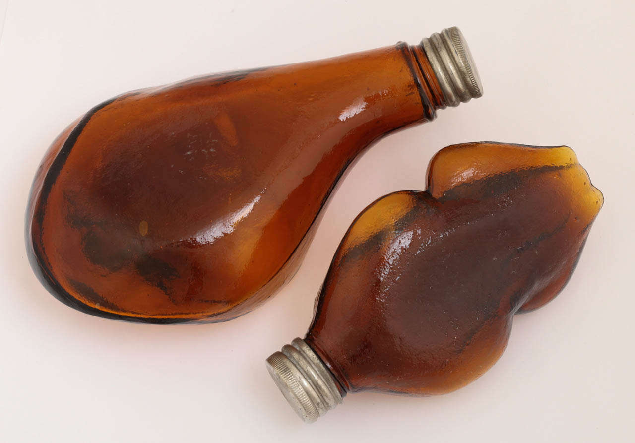 An interesting pair of bottle flasks molded in the form of a turkey (or chicken) and a ham bone. The handblown glass has a slight mottled texture and is a beautiful shade of amber. The screw top metal lids are original and in good working condition.