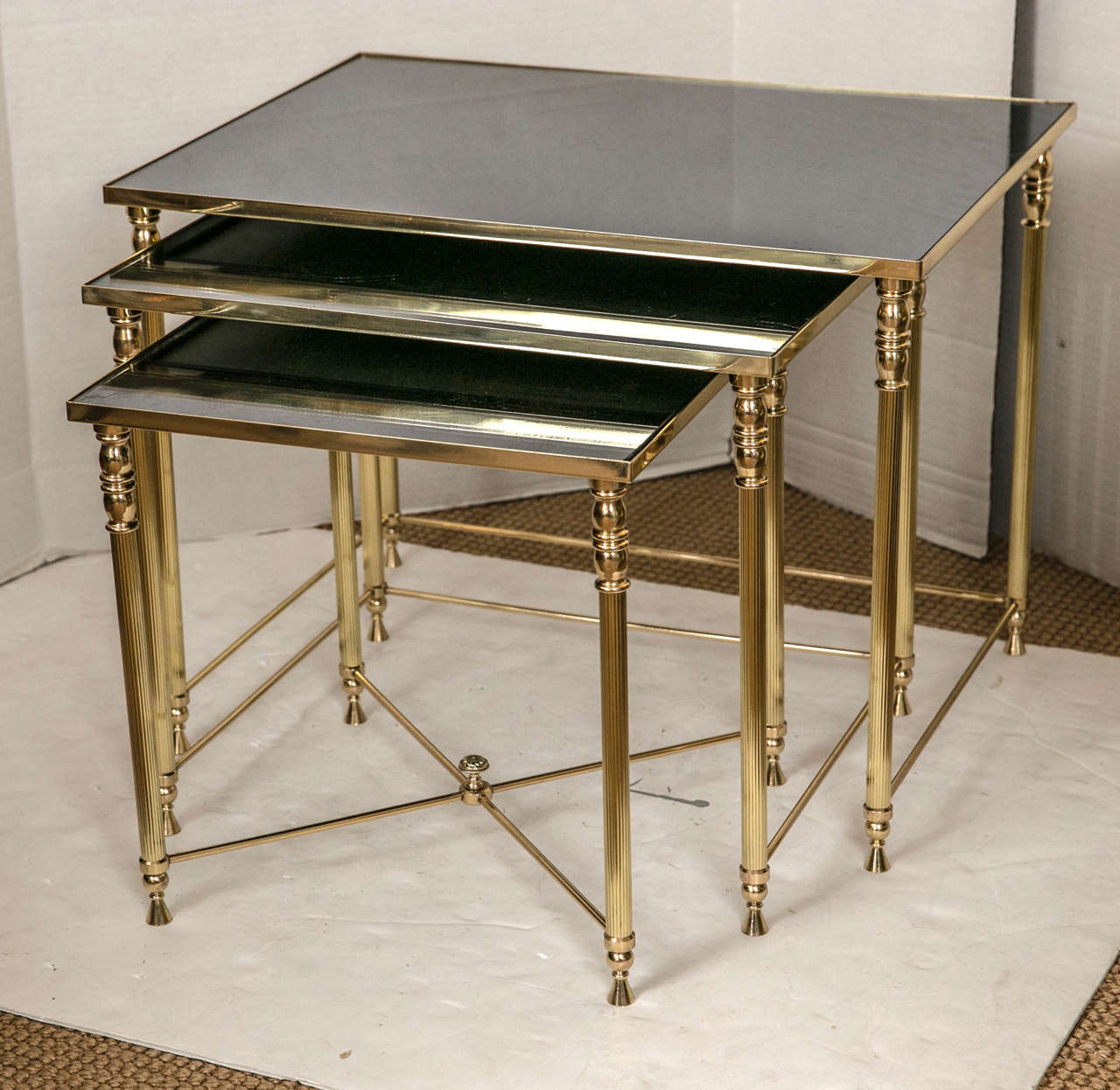 A group of three French brass and antique black mirrored glass nesting or stacking tables. Delicate tapered and fluted legs and an X-stretcher with a finial on the smallest table.
All brass has been professionally polished and clear lacquered.