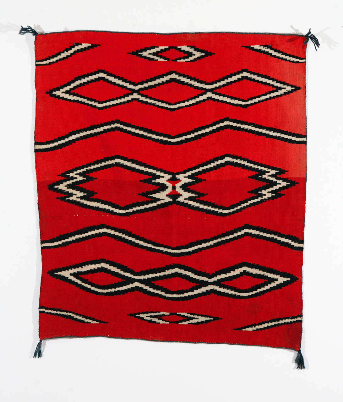 A small Navajo Child's Blanket in a serrated diamond pattern of aniline red hand spun wool, natural white hand spun, and indigo blue dyed hand spun wool.  There have been small, professional repairs by others.  The overall condition is very good. 