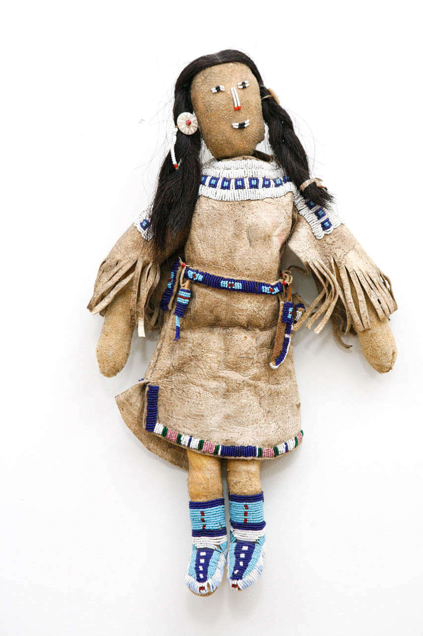 Child's doll with fringed and beaded deerskin dress, with horsehair braids and beaded belt, knife sheath and moccasins. Excellent reproduction of Native American plains style toy representing a highly decorated Indian girl.