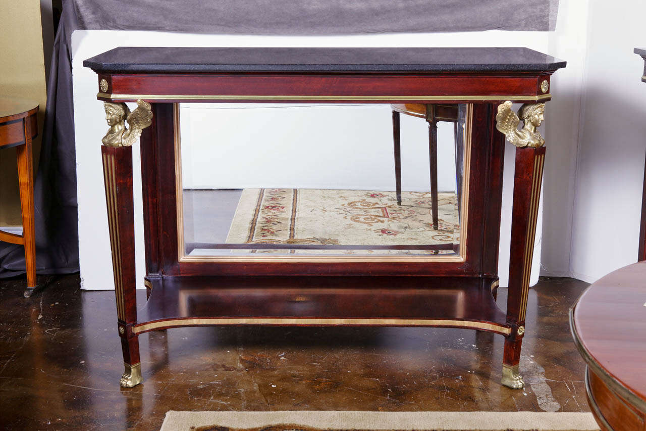 pair of early 19th c Continental mahogany and gilt bronze mounted consoles. The consoles have mirrored backs and black marble tops.