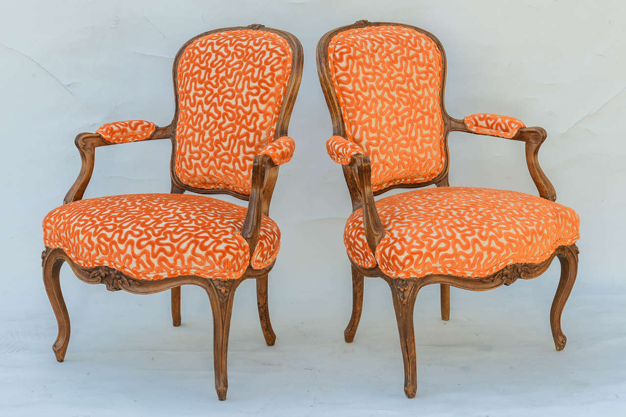 Pair of armchairs, of walnut; each having a molded carved frame, with padded shield form back, its crestrail carved with flowers, extending to scrolling arms with padded elbow rests, on downswept termains, stuff-over seat on serpentine seatrail