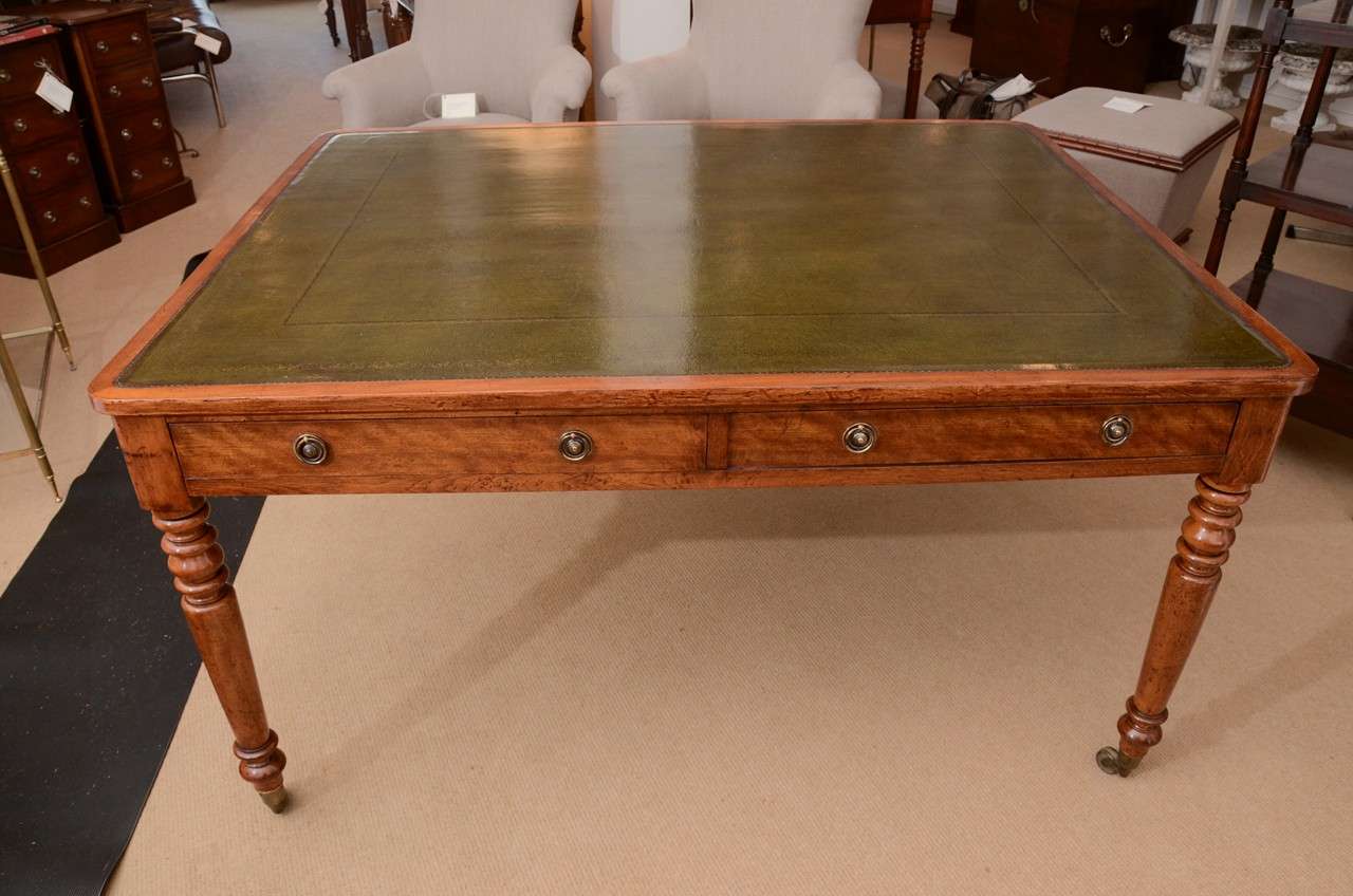 A two-drawer library writing table, beautifully restored in nicely-grained birch with molded edge, olive-green antique leather top, gilt tooling, brass ring handles, turned legs with brass castors. Knee height is 23 1/2