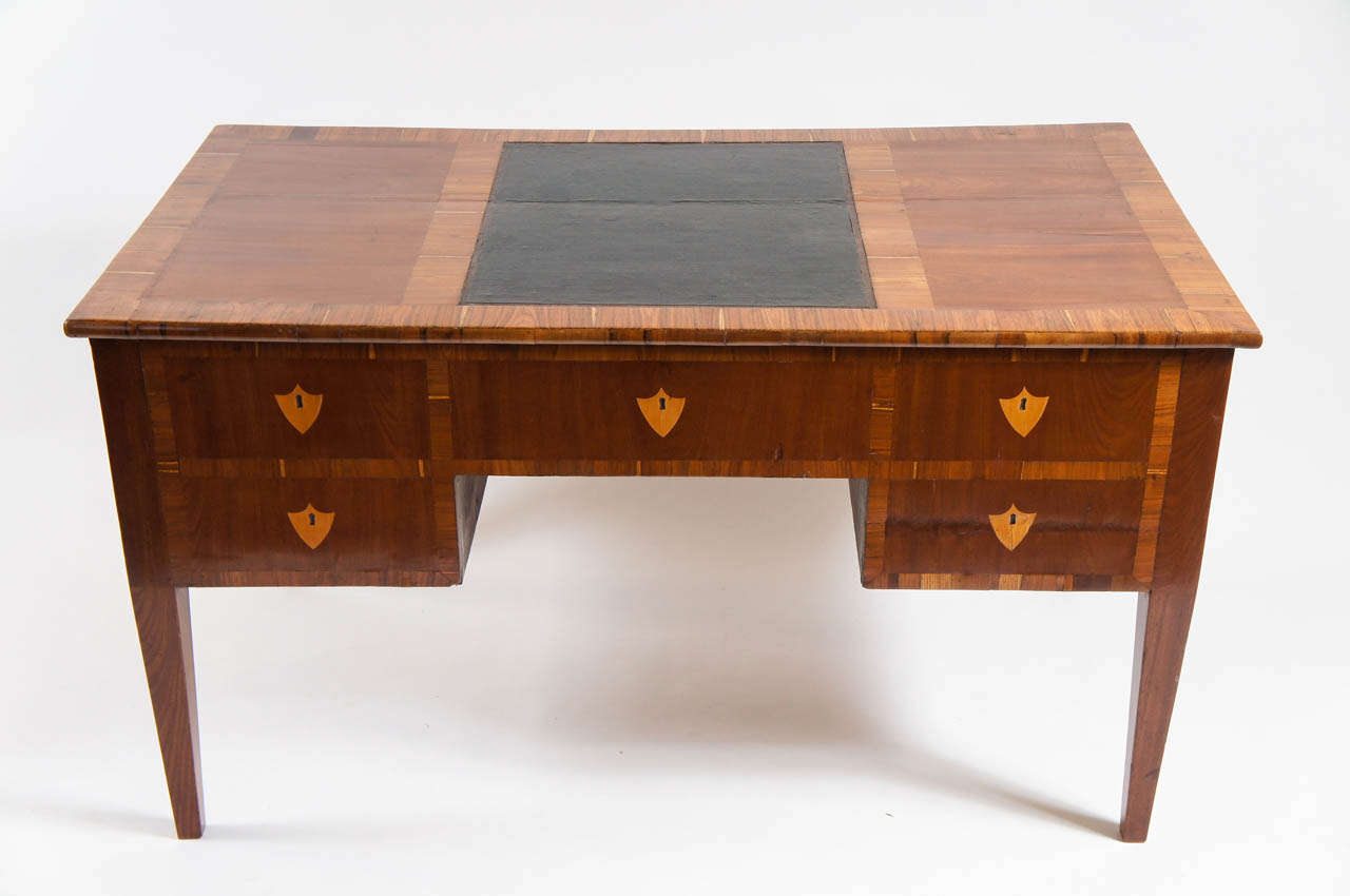 Elegant early 19th century northern Italian Biedermeier desk or bureau plat of solid mahogany frame with blonde striated fruit wood inlay borders on top and sides and shield form escutcheons on both sides with original central leather top inlay