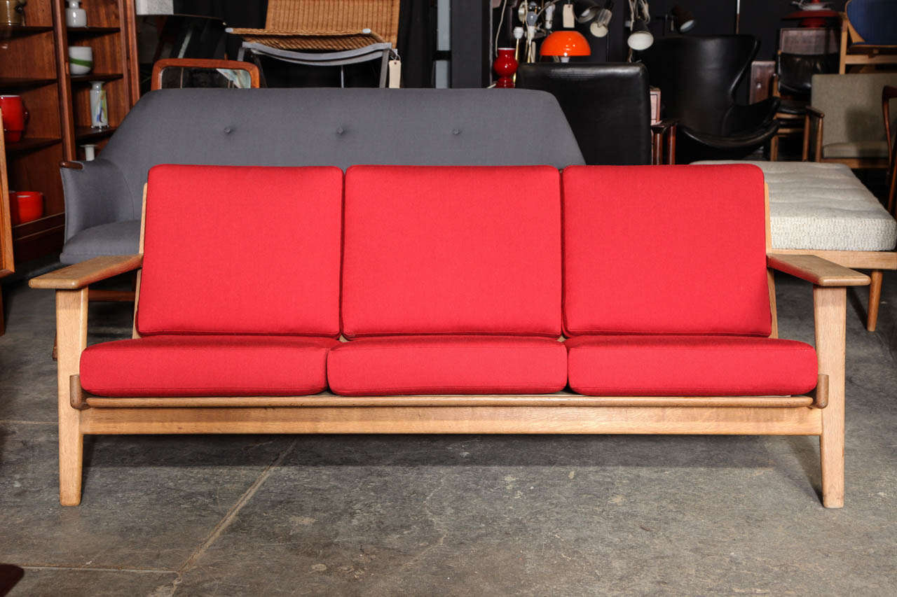 Ergonomically-designed Oak Paddle Arm Sofa by Hans Wegner. Manufactured by Getama, and features an exposed ladder back and spring cushions.  Newly upholstered in red Danish wool fabric.