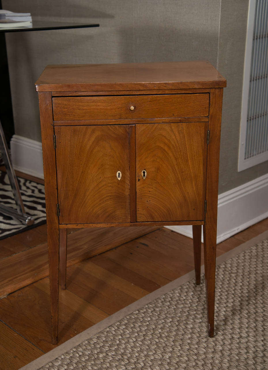 A charming French fruitwood stand with one drawer over two doors and a lower storage cabinet.  This lovely gem has ivory accents and is raised on tapered legs.