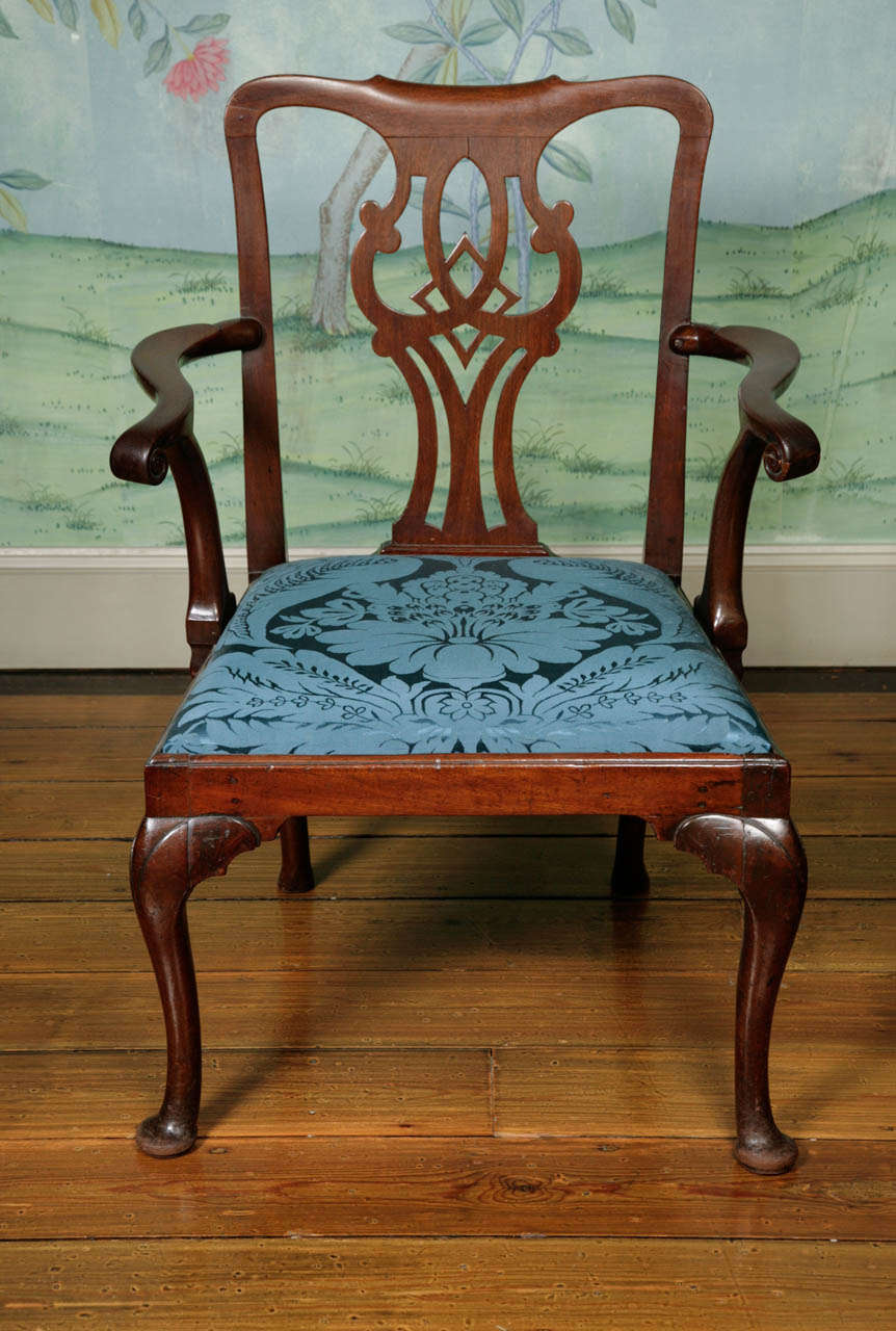 A George II mahogany open armchair with lovely scrolling arms on cabriole legs ending in pad feet. Scrolling top rail above an vase fretwork back splat. The armchair has a drop-in seat newly upholstered in blue Claremont damask. This arm chair would