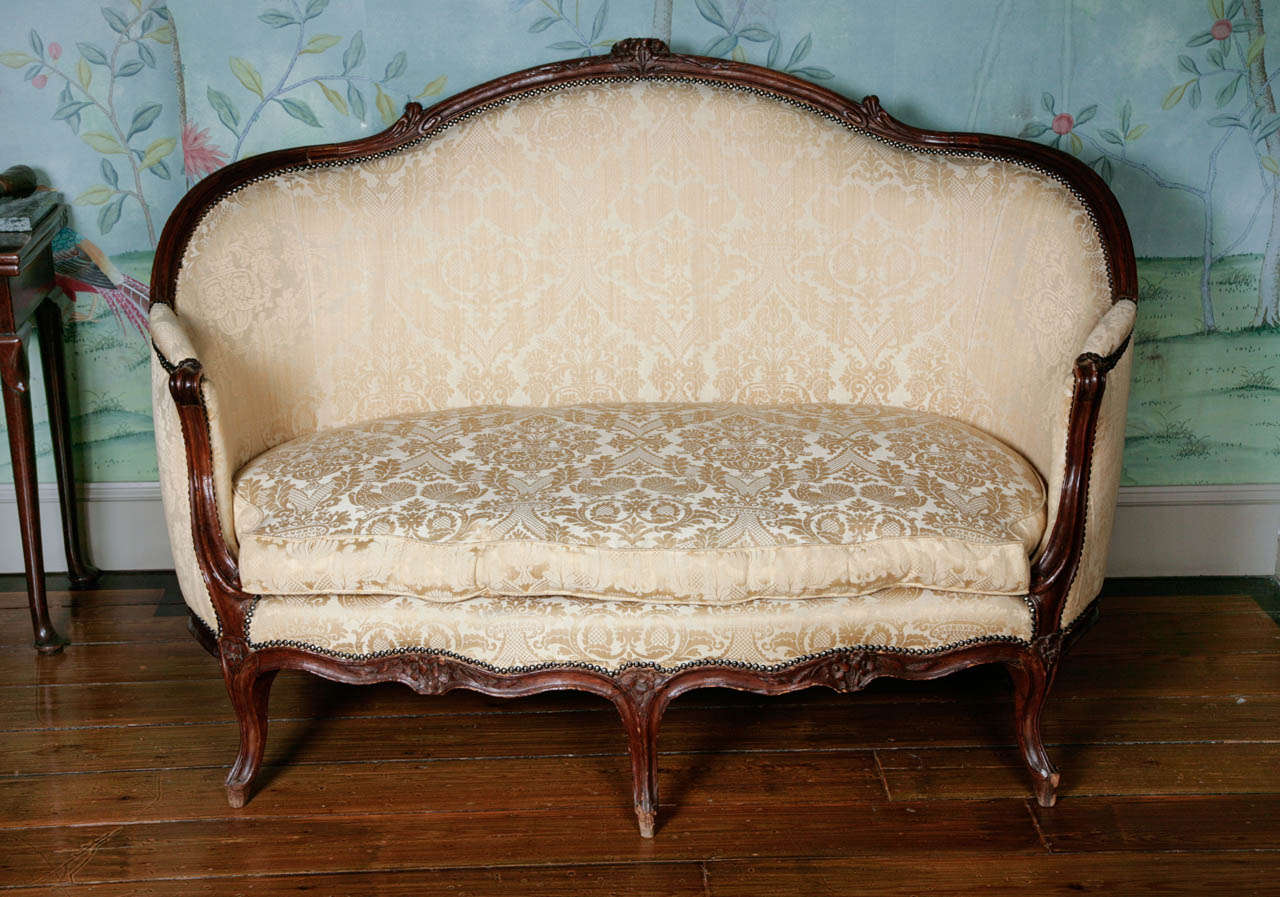 A charming French mid 18th century sofa 'en corbeille'. The serpentine-shaped back, curved sides and seat carved with flowerheads and foliage, covered in beige/yellow damask fabric, the arched cresting and shaped seat centred by floral sprays, on