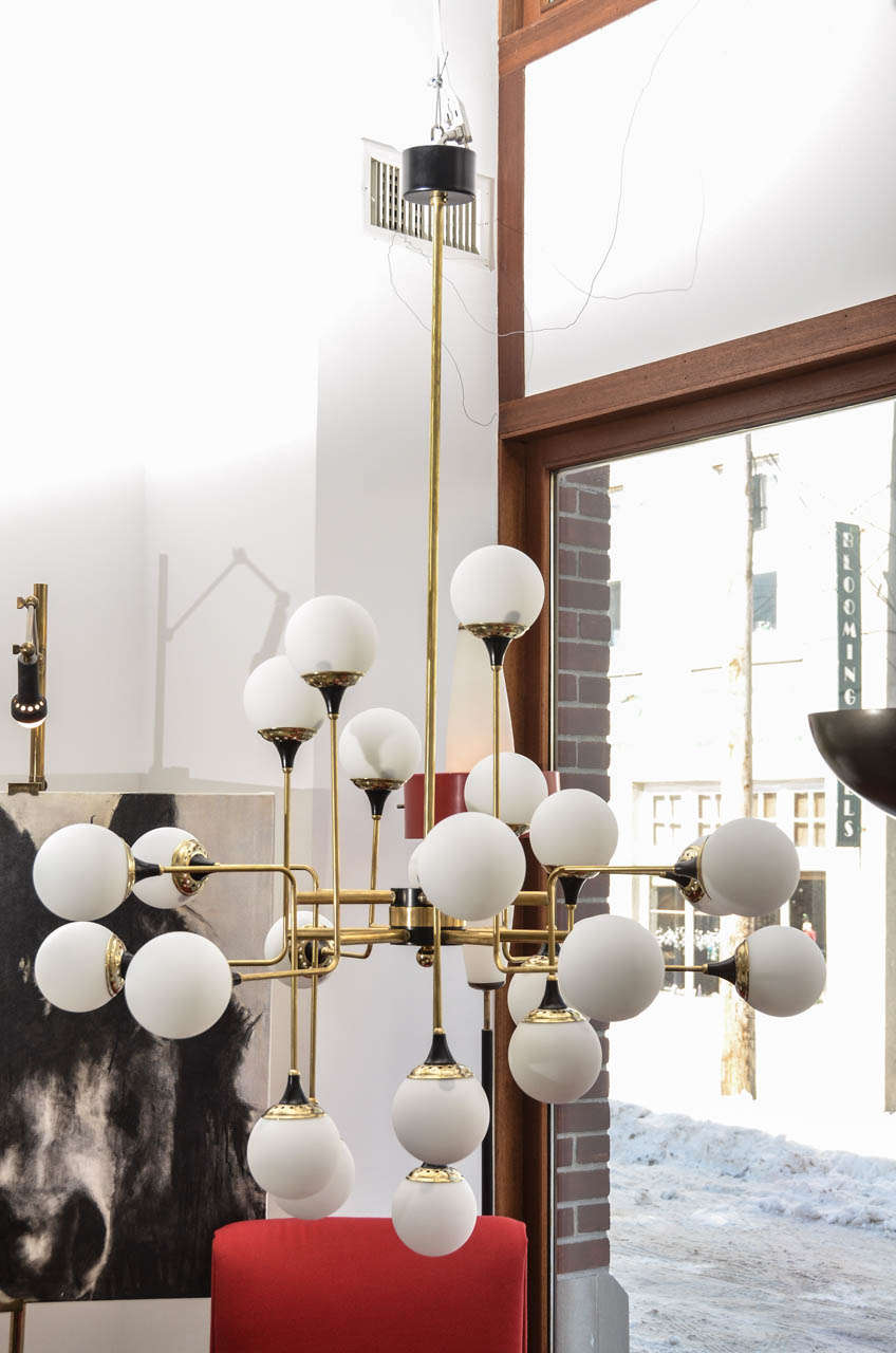 This grand scaled chandelier has 12 brass bent arms and 24 lights with round white handblown globes.  Created in the mid-century Stilnovo style it reflects the asymetric character of the modern age.  All un-lacquered brass with black enamel