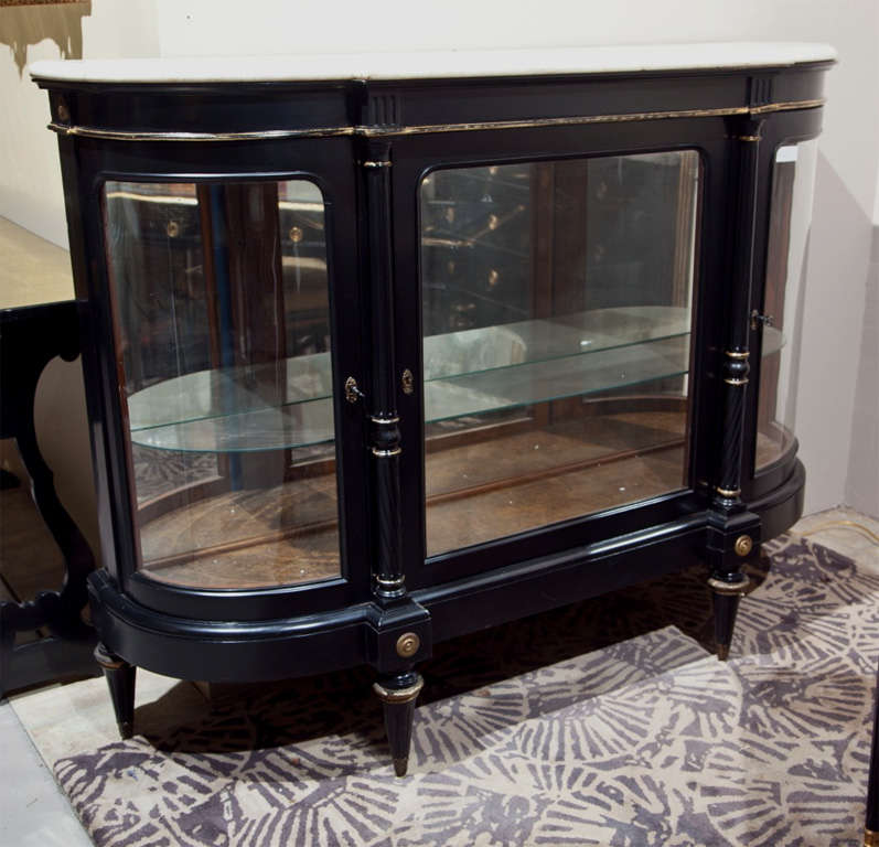 French Directoire style curio cabinet, circa 1940s, the white half-moon marble atop a conforming ebonized cabinet with glass front, the center door flanked by circular columnar uprights, raised on four tapering bulbous legs. Stamped Jansen.