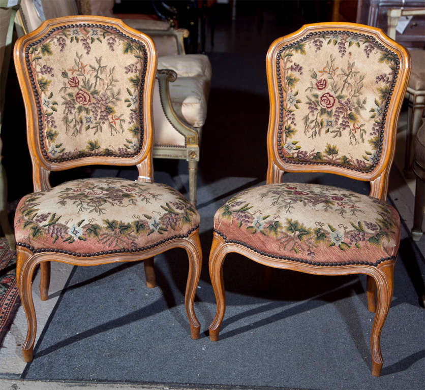 Pair of French Louis XIV style distressed walnut side chairs, 20th century, each with needlepoint upholstered back and seat decorated with nail heads, raised on cabriole legs.