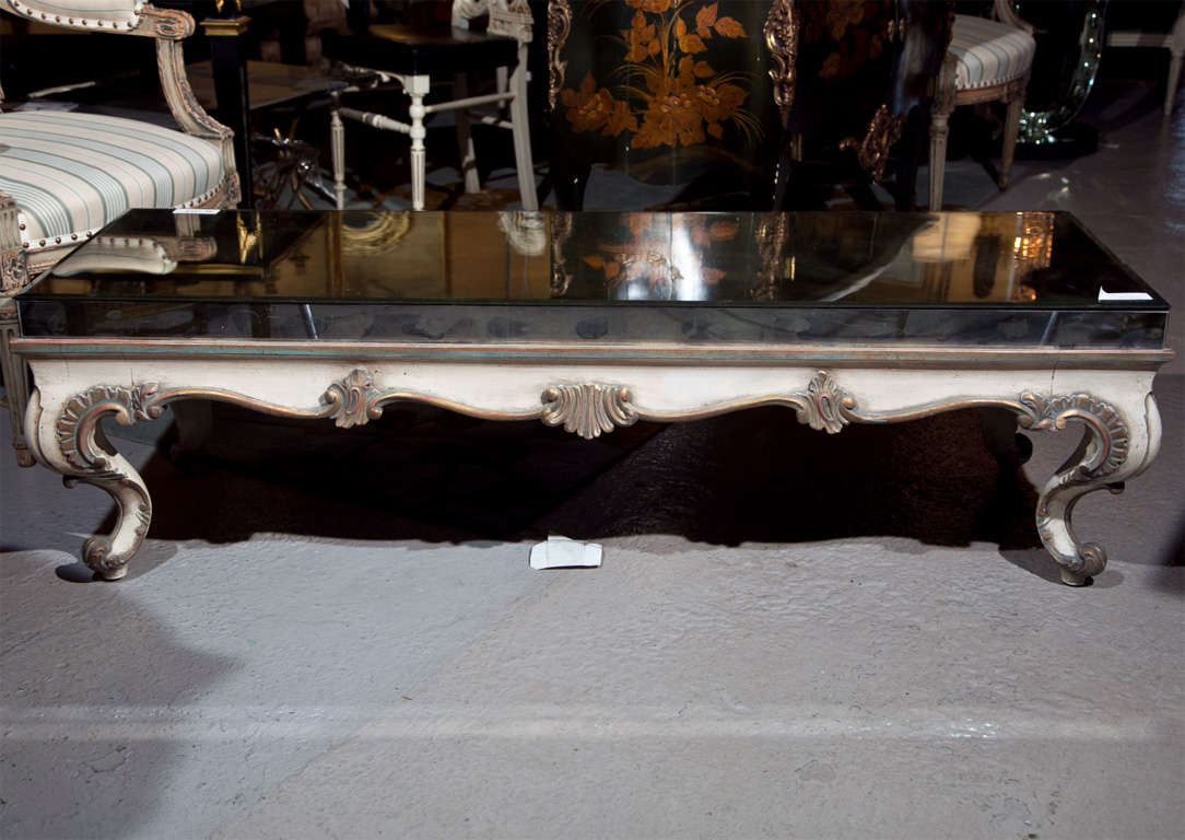 An attractive polychromed coffee table in the taste of French Rococo, circa 1940s, raised distressed mirrored top over a scalloped apron decorated with shell crest, raised on cabriole legs. By Maison Jansen.