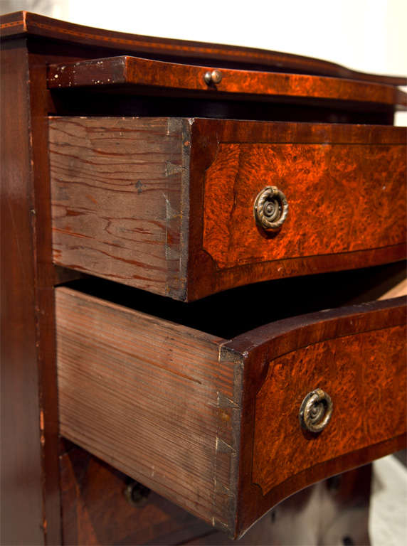Pair of Sheraton style mahogany bachelor's chests of drawers, serpetine top with burled banding over a narrow pull-out slide and a conforming case fitted with four burled drawers, raised on a scalloped apron and splayed legs.