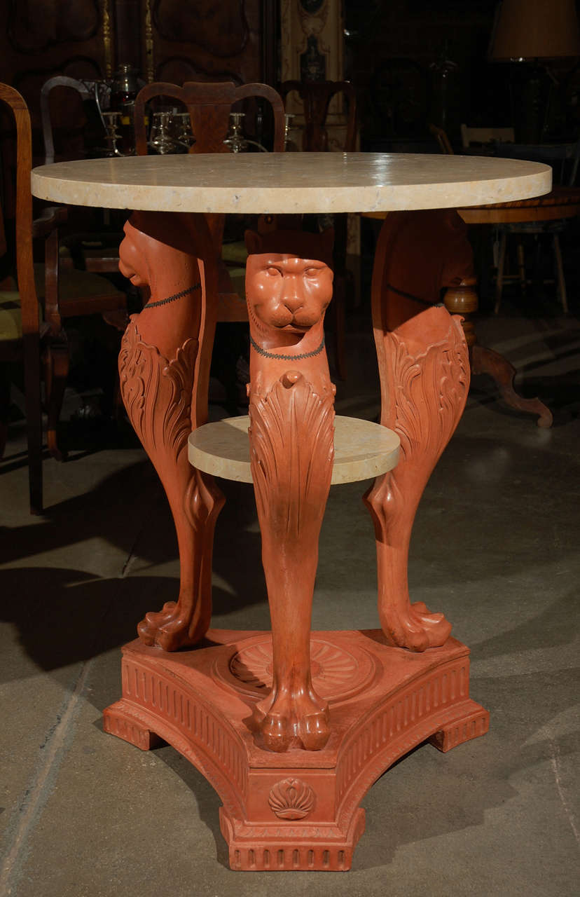 Pair of impressive terra cotta Egyptian Revival pedestal tables, thought to be Italian, circa the 1930's, having marble tops along with a lower marble shelf. The three legs have lion heads with acanthus leaf shield decorative elements and end in