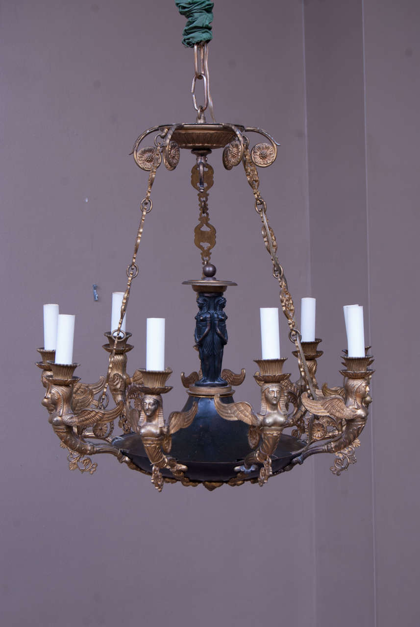 This Napoleonic chandelier was probably made in Paris and is remarkably intact for its age. It has the three graces in the center and caryatids for candle arms. The center bowl is adorned with an acanthus leaf circular mount. The beautiful chain as