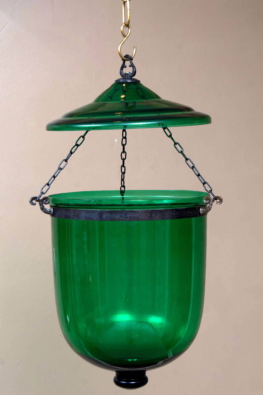 This bell jar lantern is in hand-blown glass in a rich green. Hand-forged aged brass hardware. Electrication will be with a 3-light cluster on a rod down from the smoke plate. Total height is adjustable prior to wiring, if desired. Hanging hardware