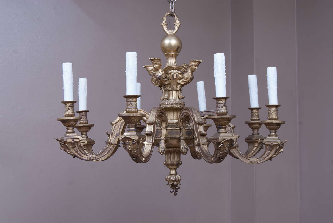 This impressive chandelier was hand-cast and hand-constructed, probably in France in the latter 19th century. It features winged caryatids on the stem and Neptune's face below the bobeche on each arm. Rich gilt bronze finish, bellflower finial,