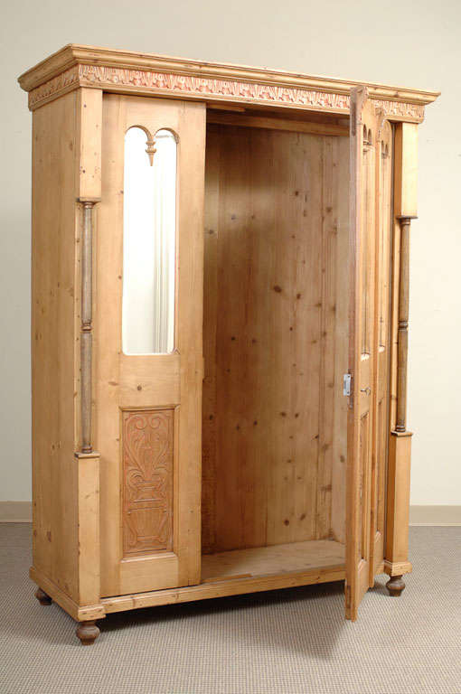 A mirrored wardrobe with one double width and one single width door. The carved frieze and panels with remnants of old red undercoat flanked by beechwood balusters ending in turned wooden feet.