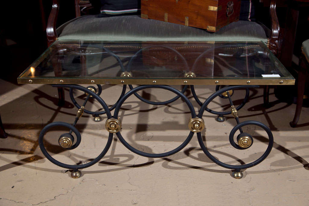 French Directoire style coffee table in the manner of Jansen, 20th century, the rectangular glass top with bronze banding and rivet-decoration, atop a scrolled metal base decorated with brass accents. In the manner of Jansen.