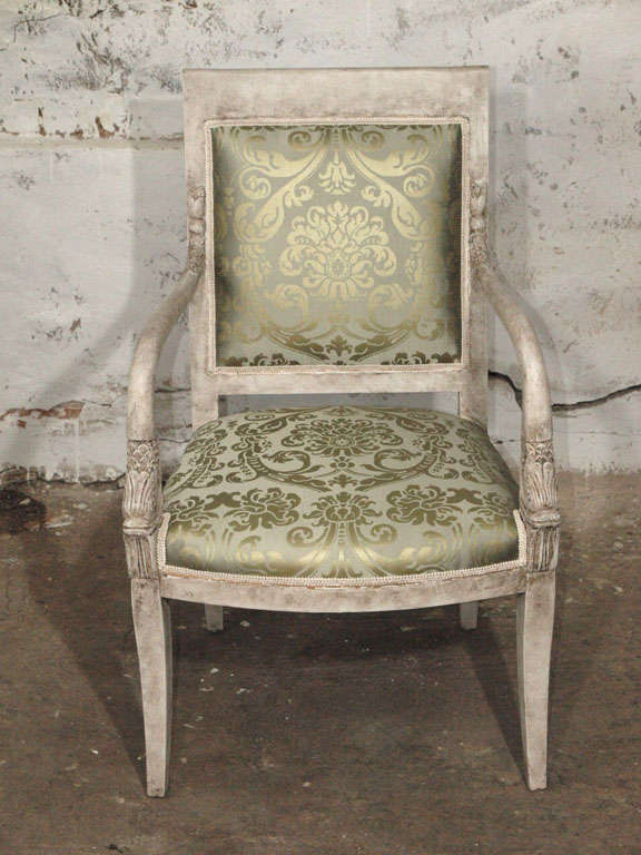 Impressive pair of Empire or Neoclassical armchairs with carved dolphins at the forefront of the arms and acanthus leaves on back rest. Newly upholstered in an elegant imported hand printed Italian silk (Fortuny style) in hues of gold over a pale