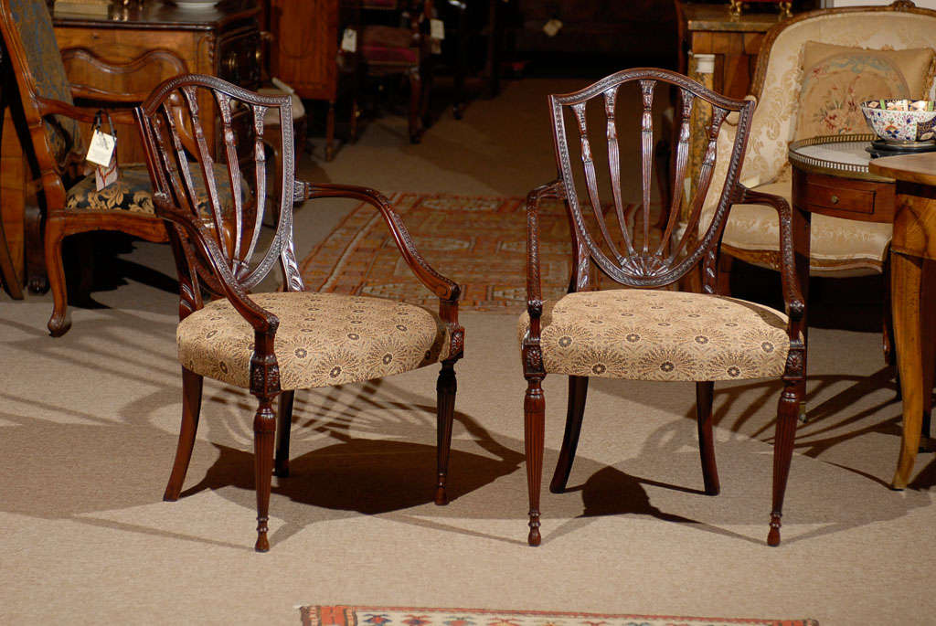 A pair of Englsih Hepplewhite style mahogany arm chairs with shield shape backs with railed splats, down swept arm supports and upholstered seat on tapering  reeded circular legs with paterae.  

William Word Fine Antiques: Atlanta's source for