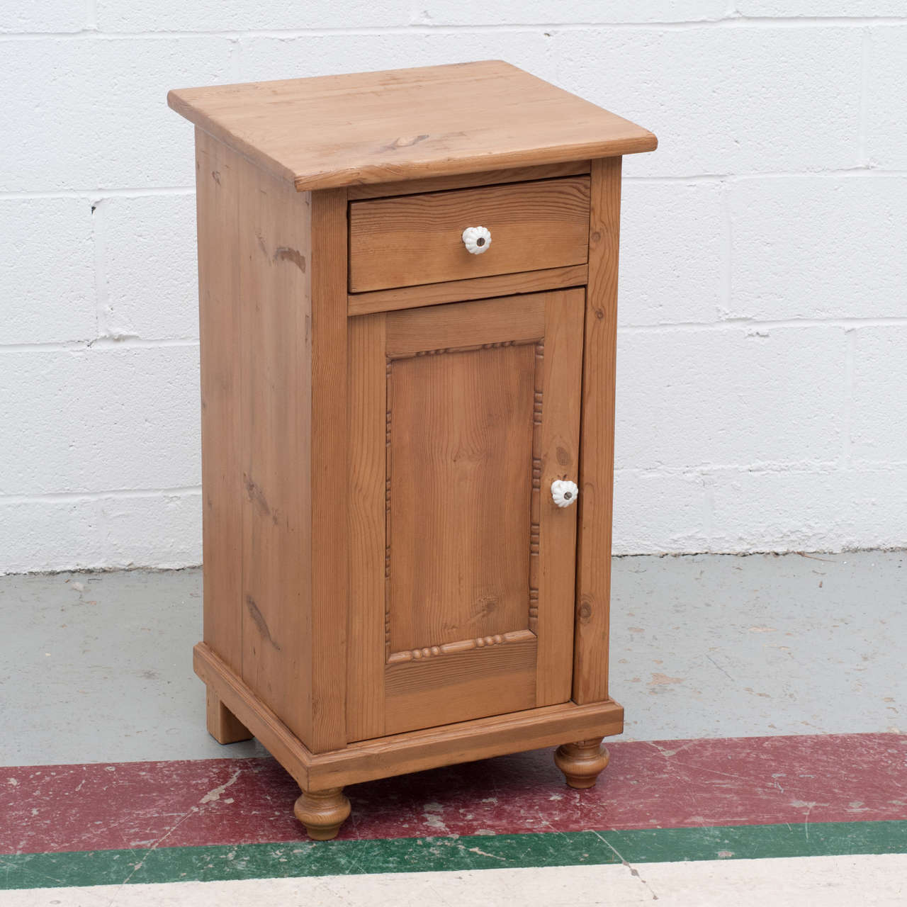 A single small pine nightstand with one door with beaded molding to the panel and one hand-cut dovetailed drawer.  Original ceramic knobs.  Single shelf inside.