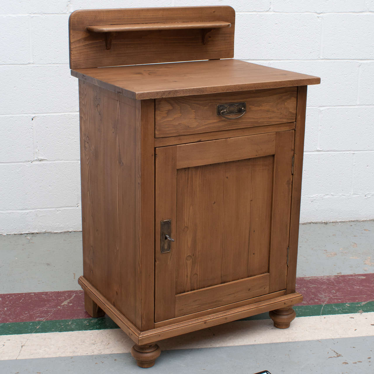 A small and versatile pine single door base, nightstand, or washstand with splashback gallery and shelf.  One hand-cut dovetailed drawer and one interior shelf.