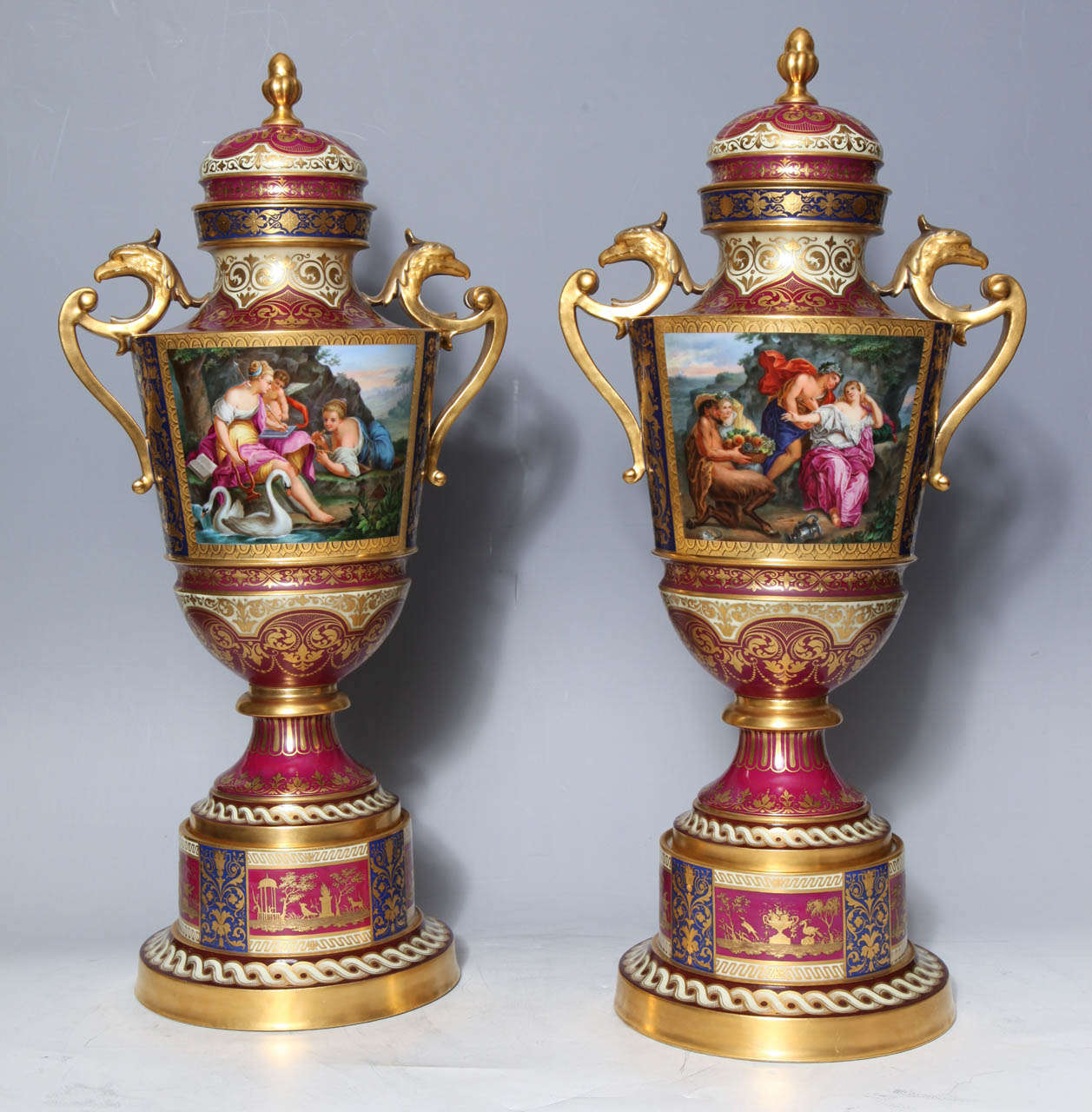 A magnificent pair of 19th century royal Vienna covered urns on original stands with double eagle handles depicting neoclassical lovers and cupid. These ornate urns show scenes populated by angelic cupids in beautifully deep landscapes surrounding