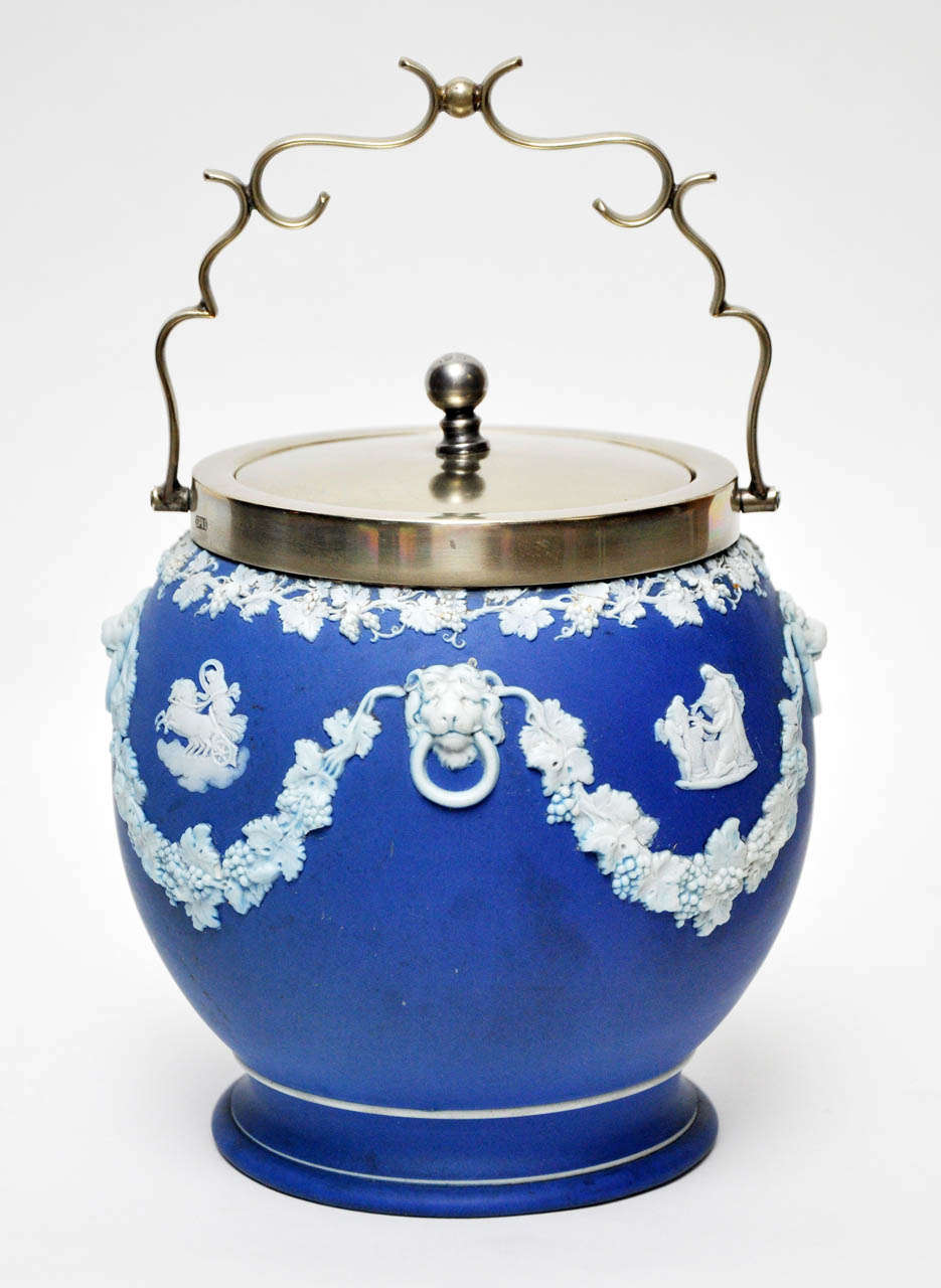 Wedgwood jasperware biscuit jar, blue ground with white ceramic cameo figure, lion and garland reliefs.  EPNS silver lid, scrolled handle. Signed with Wedgwood markings.