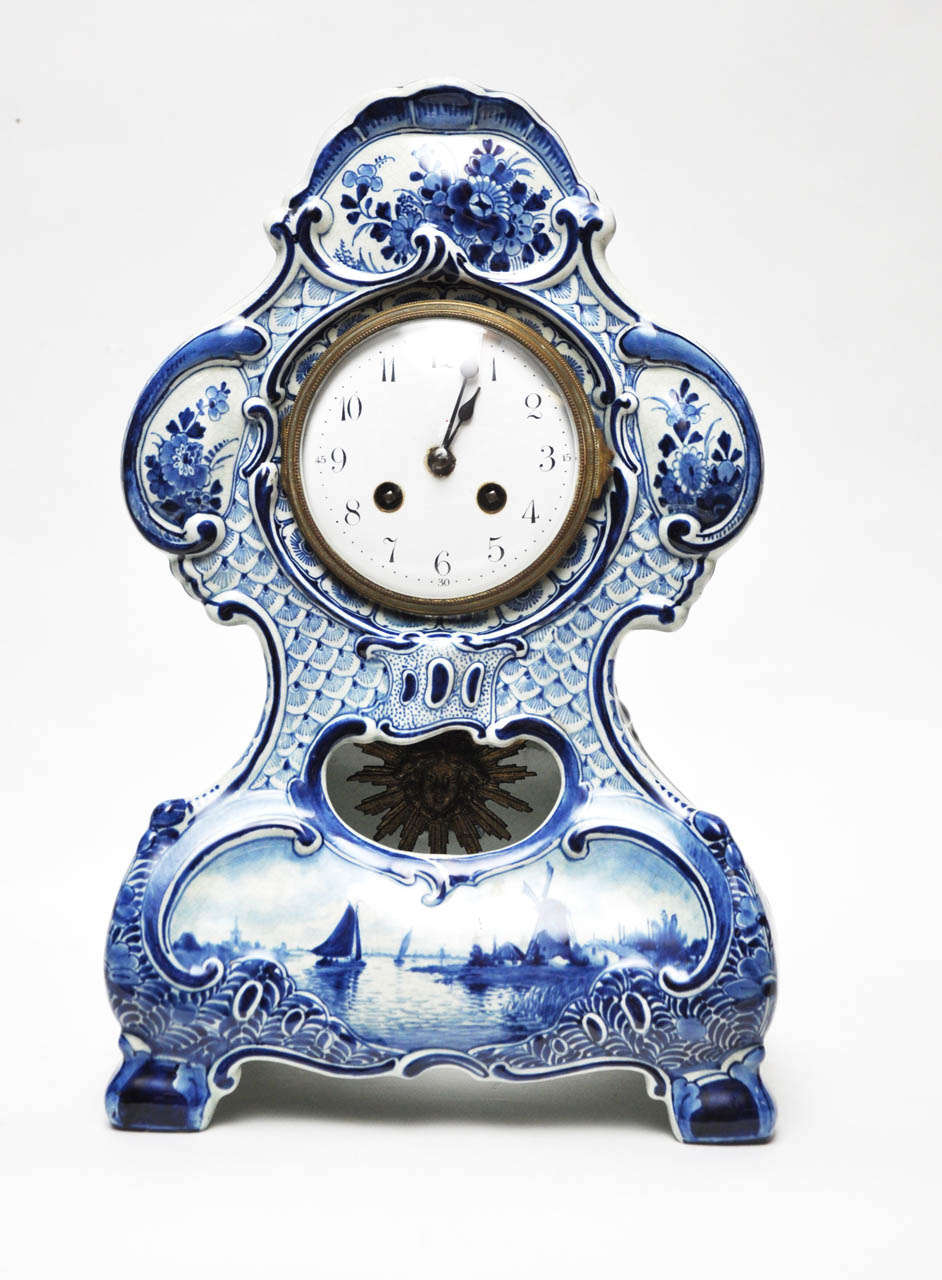 Charming porcelain, blue and white mantel clock, signed Delft (on inside center just behind pendulum). The clock case with undulating shape, decorated with hand-painted Delft blue and white floral design frames hinged glass door which reveals white