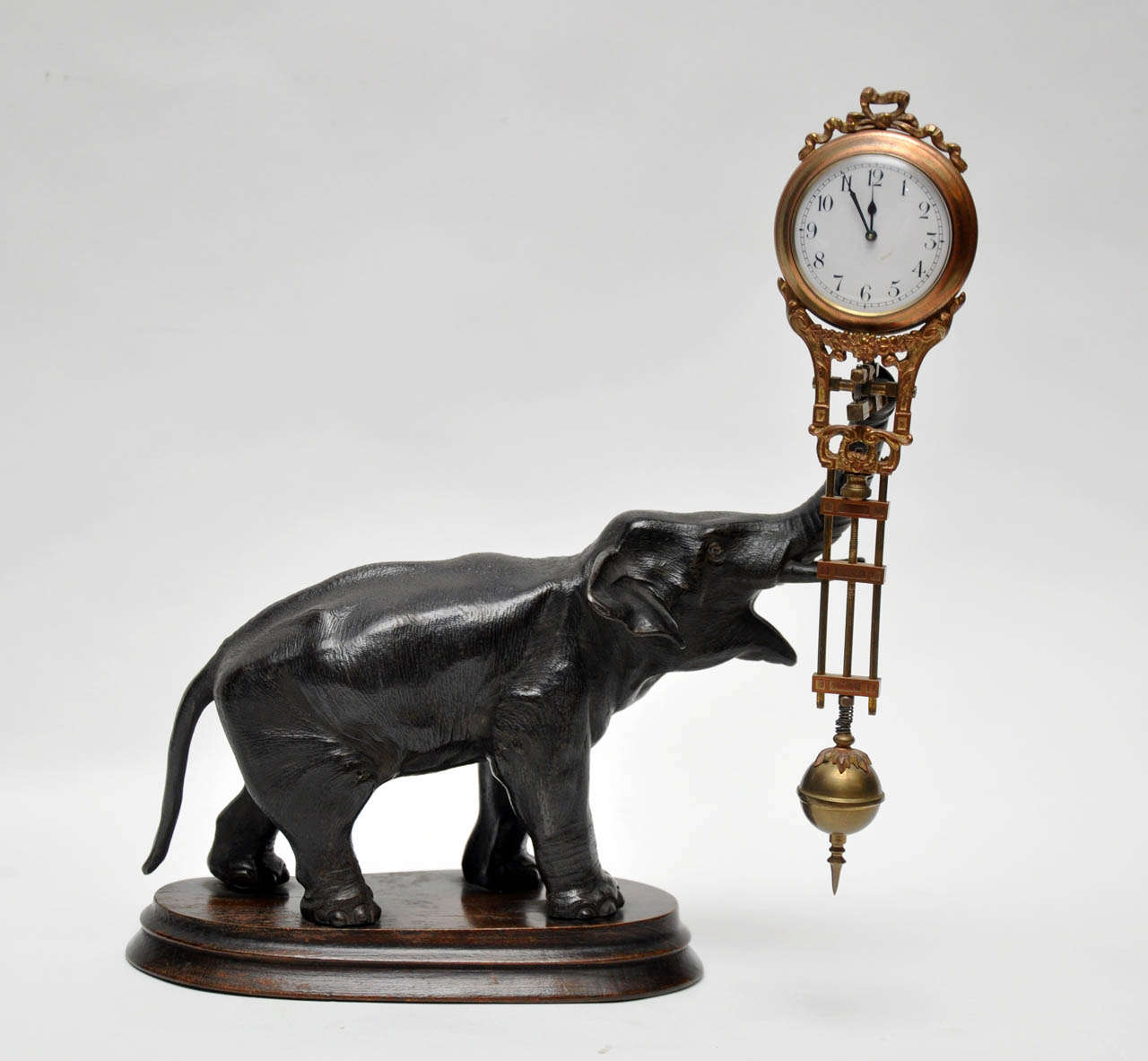 Rare French  bronze figure of an elephant on a carved wooden oval base. A brass lyre shaped pendulum swings from the elephant's trunk. White porcelain dial, black Arabic numerals, black spade hands, eight day, pinwheel movement. Jungham clock,