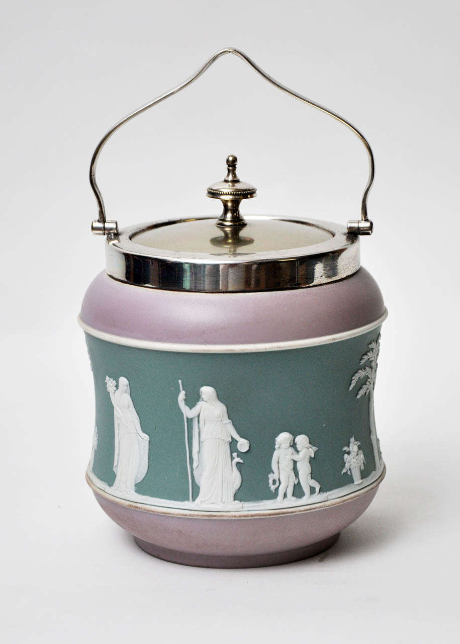 A charming tri-colored lavender and green, trimmed in white biscuit jar, raised white figures of women, cupids and floral encircle the center. Epns silver lid, rim and arched handle. Marked on bottom, Wedgwood, England, Buslem England.