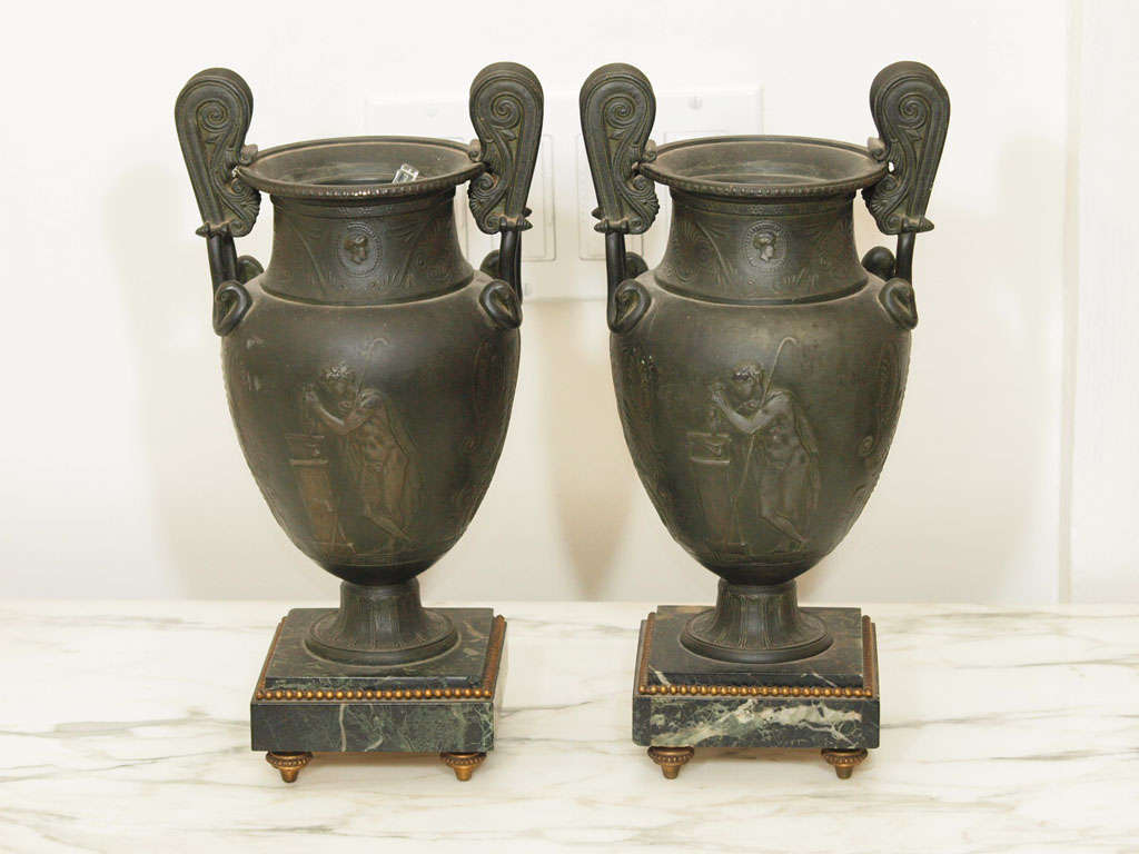 Two Neo-classical urns with decorations in the classical taste; each resting on a square marble base with gilt detailing and feet